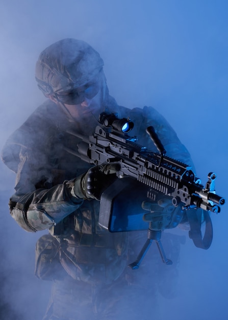Porträt eines Airsoft-Spielers in professioneller Ausrüstung mit Maschinengewehr in verlassenen Gebäuderuinen. Soldat mit Waffen im Krieg in Rauch und Nebel