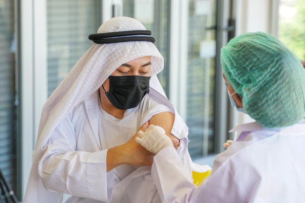 Porträt eines arabischen muslimischen Mannes, der sich ansieht, während er in einer Klinik oder einem Krankenhaus einen Covid-Impfstoff erhält, wobei die Handkrankenschwester den Impfstoff injiziert, um Immunität zum Schutz des Virus zu erhalten. Menschen, die eine Schutzmaske tragen.