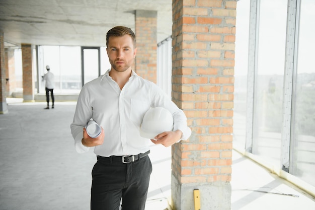 Porträt eines Architekten, der den Grundriss der Räume studiert, ein seriöser Bauingenieur, der mit Dokumenten zum Baustellenbau und zur Hausrenovierung arbeitet, professioneller Vorarbeiter bei der Arbeit