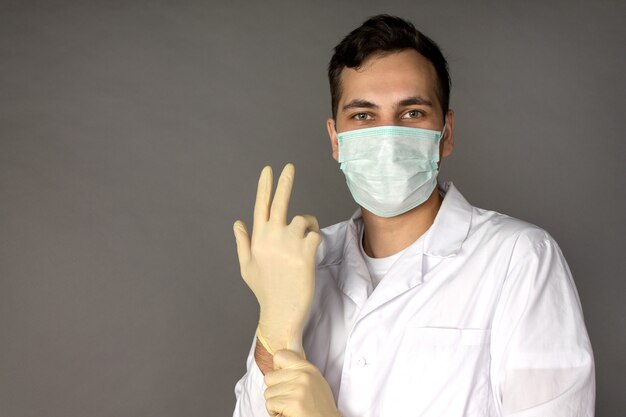 Porträt eines Arztes in einem medizinischen Gewand, der Handschuhe anzieht, bevor Tests auf Coronavirus durchgeführt werden