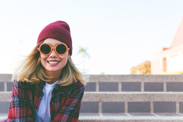 Porträt eines asiatischen Hipster-Mädchens mit orangefarbener Sonnenbrille im Vintage-Stil. Lebensstil einer einzelnen jungen Frau. Mode-Indy-Stil-Konzept