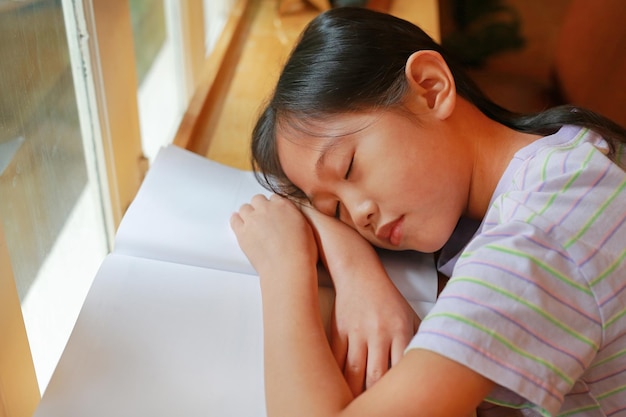 Foto porträt eines asiatischen jungen mädchens, das auf einem buch in der nähe der fenster schläft bildungs- und ruhekonzept