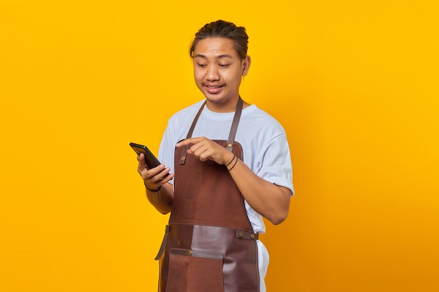 Porträt eines asiatischen jungen Mannes mit Schürze überrascht, eine eingehende Nachricht auf dem Smartphone zu sehen