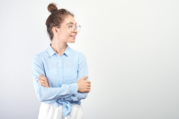 Porträt eines asiatischen kasachischen Studentenmädchens mit Haarknoten auf dem Kopf und Brille mit verschränkten Armen lächelnd und zur Seite schauend mit Kopierraum auf weißem Hintergrund