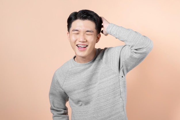 Porträt eines asiatischen Mannes, der sein Haar berührt und auf beigem Hintergrund lacht
