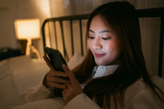 Porträt eines asiatischen Teenager-Mädchens, das nachts im Bett liegt und ein Smartphone benutzt Junge Frau, die nachts im Bett liegt und ein Smartphone für soziale Medien benutzt und Serien nachts schaut Schlaflosigkeit Schlafstörung Konzept