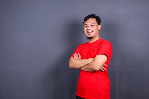 Porträt eines attraktiven asiatischen Mannes in rotem T-Shirt, der mit verschränkten Armen steht, isoliert auf grauem Hintergrund