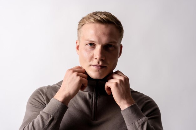 Porträt eines attraktiven blonden deutschen Models mit braunem Pullover auf weißem Hintergrund, das in die Kamera blickt