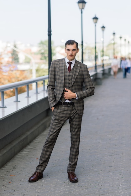 Porträt eines attraktiven jungen Geschäftsmannes im tragenden Anzug und in der Krawatte des städtischen Hintergrundes.