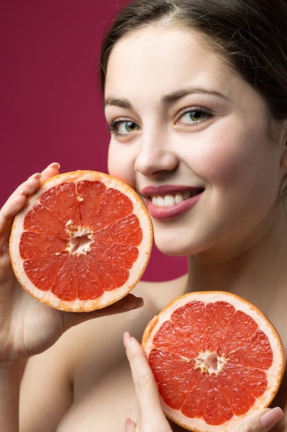 Porträt eines attraktiven Mädchens, das eine Grapefruitscheibe auf rotem Hintergrund hält