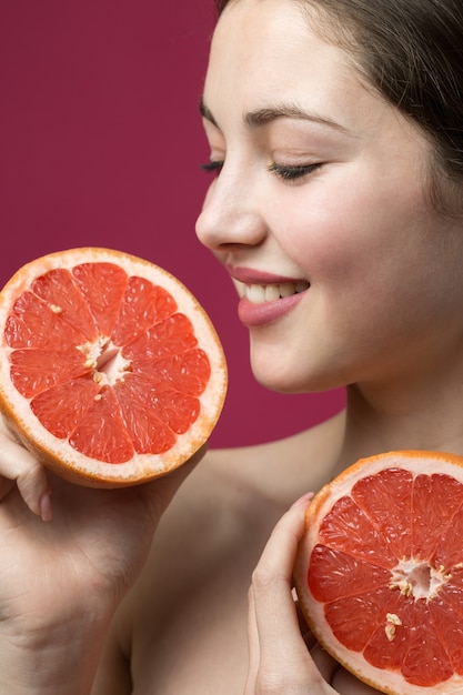 Porträt eines attraktiven Mädchens, das eine Grapefruitscheibe auf rotem Hintergrund hält