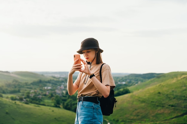 Porträt eines attraktiven Mädchens in stilvoller Kleidung, das mit einem Smartphone in der Hand auf einem Berg steht und Fotos auf einem Smartphone mit ernstem Gesicht macht Inlandstourismus Zalupne Tovtry