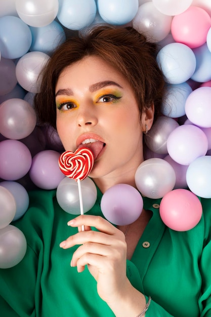 Porträt eines attraktiven, schönen Mädchens, stilvoll mit hellem Make-up und emotionalem Gesichtsausdruck aus doppeltem Dutthaar, das in einem Pool liegt, der mit pastellfarbenen bunten Plastikbällen gefüllt ist, Draufsicht