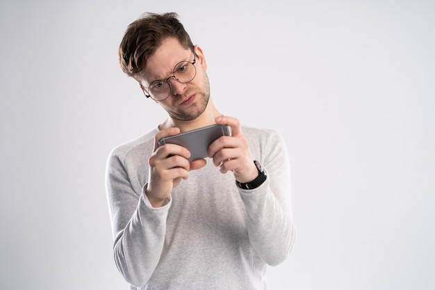 Porträt eines aufgeregten jungen Mannes im weißen T-Shirt, das Spiele auf Handy spielt