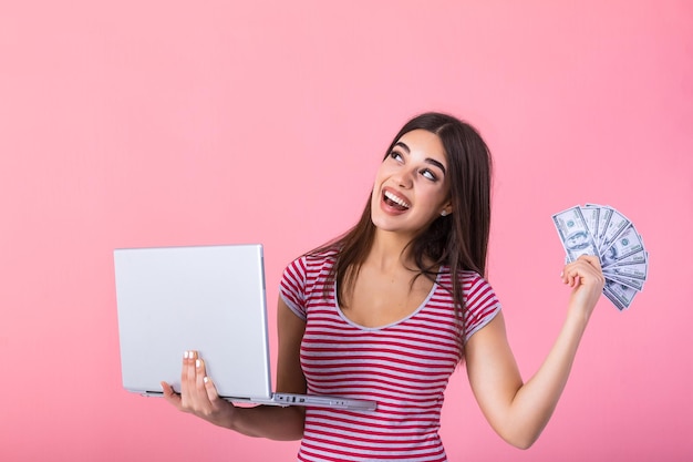 Porträt eines aufgeregten, zufriedenen Mädchens, das Geld, Banknoten und Laptop in der Hand hält. Glückliche Frau mit glücklichem Geld Foto einer schönen Frau mit Laptop, isoliert auf rosa Hintergrund