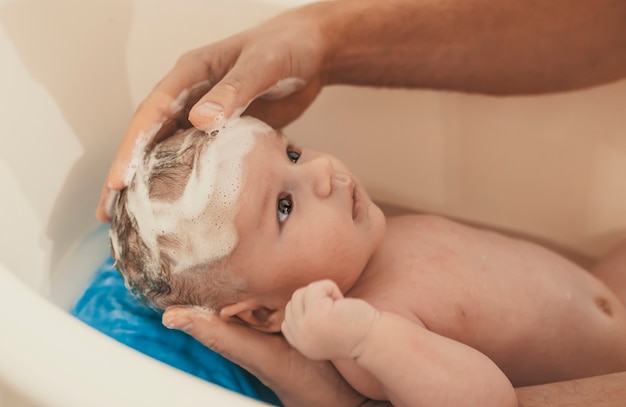 Porträt eines Babys wird von seinem Vater gebadet, der zu Hause Wanne verwendet