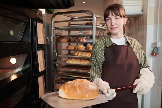 Porträt eines Bäckers, der in die Kamera schaut, während er frisches Brot aus dem Ofen nimmt