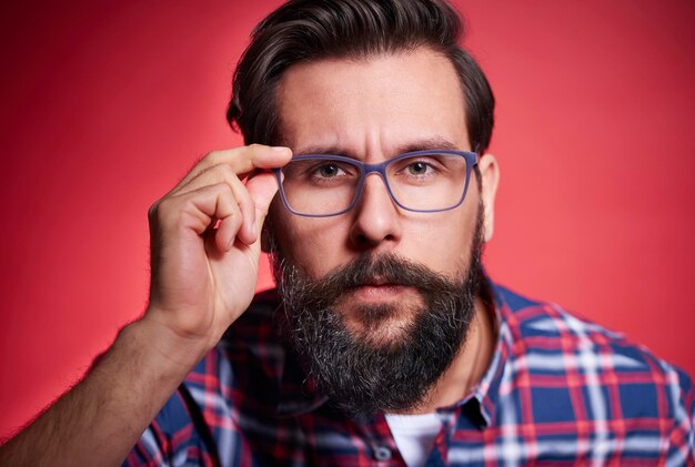 Porträt eines bärtigen jungen Mannes, der eine Brille gegen einen farbigen Hintergrund trägt