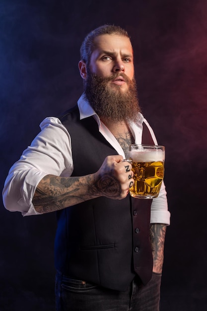Porträt eines bärtigen Mannes, der einen Krug Bier hält und vor schwarzem Hintergrund in die Kamera blickt