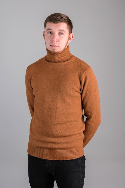 Porträt eines bärtigen Mannes, der in einem roten Pullover mit den Händen hinter dem Rücken auf grauem Hintergrund steht