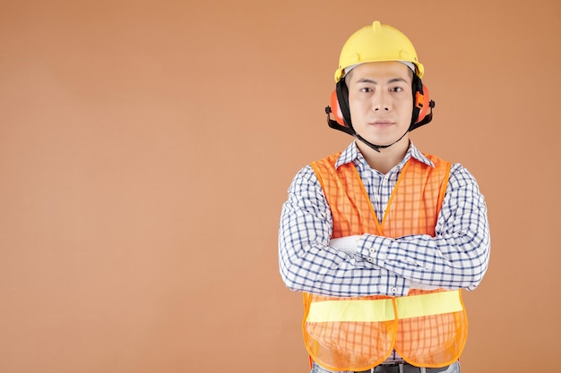 Porträt eines Bauarbeiters in heller Weste und Ohrenschützern, die Arme kreuzen und in die Kamera schauen
