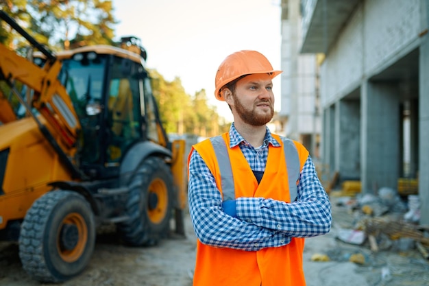 Porträt eines Bauunternehmers, der auf der Baustelle vor schweren Maschinen des Traktors steht