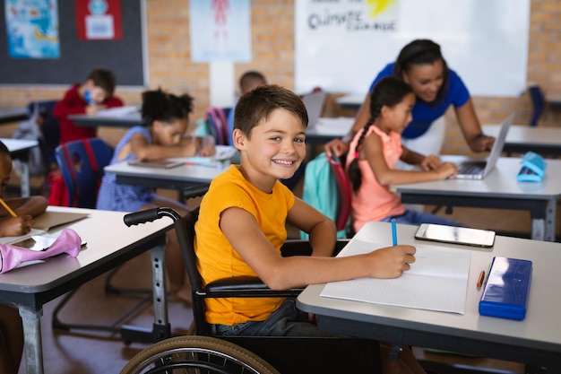 Porträt eines behinderten kaukasischen Jungen, der lächelt, während er in der Grundschule im Rollstuhl sitzt