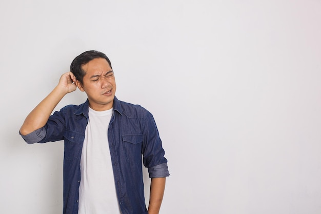 Porträt eines beiläufigen asiatischen Mannes, der sich mit verwirrtem Ausdruck auf weißem Hintergrund die Haare kratzt