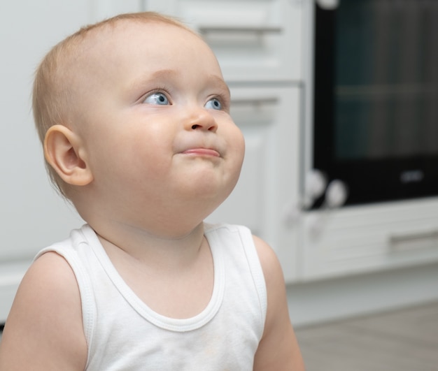 Porträt eines blonden Babyjungen mit großen blauen Augen in umweltfreundlichen Materialkleidung zu Hause.