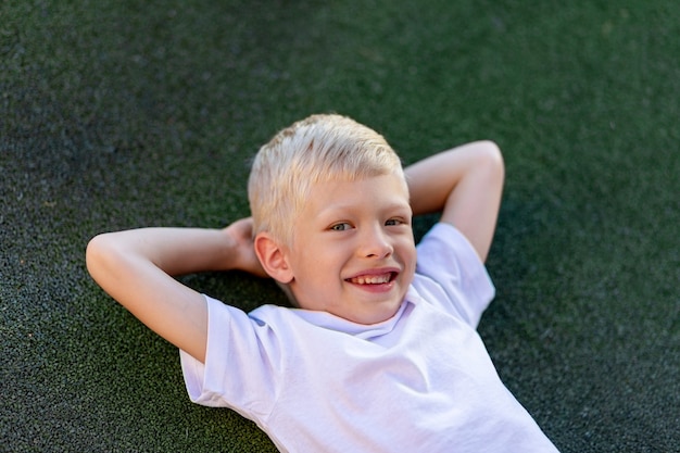 Porträt eines blonden Jungen in einer Sportuniform, die auf dem Fußballplatz liegt