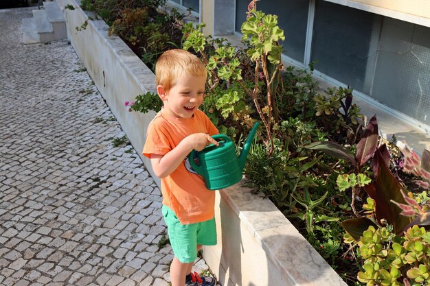 Foto porträt eines blonden jungen mit einer bewässerungsdose, ein vierjähriger junge lächelt und bewässert blumen