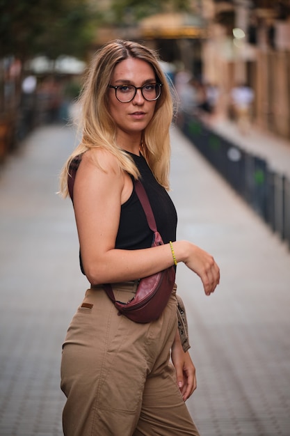 Porträt eines blonden Mädchens mit Brille, das für ein Fotoshooting auf einer Straße in der Stadt Barcelona posiert.