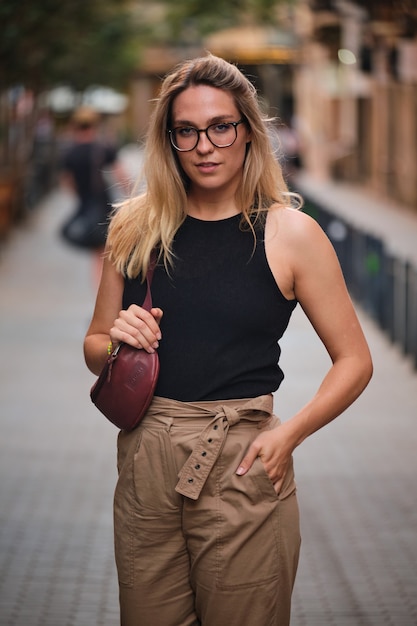 Porträt eines blonden Mädchens mit Brille, das für ein Fotoshooting auf einer Straße in der Stadt Barcelona posiert.