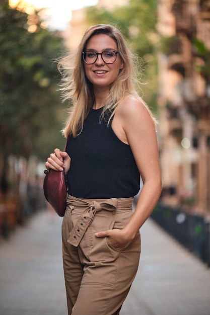 Porträt eines blonden Mädchens mit Brille, das für ein Fotoshooting auf einer Straße in der Stadt Barcelona posiert.