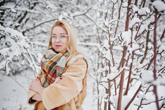 Porträt eines blonden Mädchens mit Brille, rotem Pelzmantel und Schal am Wintertag.