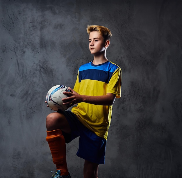 Porträt eines blonden Teenagers, Fußballspieler in gelber Uniform spielt mit einem Ball.