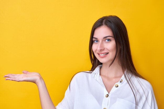 Porträt eines brünetten lächelnden Mädchens, das vorgibt, etwas auf der Handfläche zu halten, isoliert auf gelbem Studiohintergrund mit Kopierraum