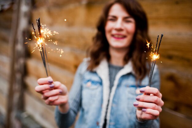 Porträt eines brünetten Mädchens in Jeansjacke mit bengalischen Lichtern in den Händen