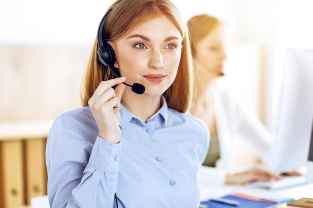 Porträt eines Call-Center-Betreibers bei der Arbeit im sonnigen Büro. Gruppe von Personen in einem Headset, die bereit sind, Kunden zu helfen. Unternehmenskonzept.