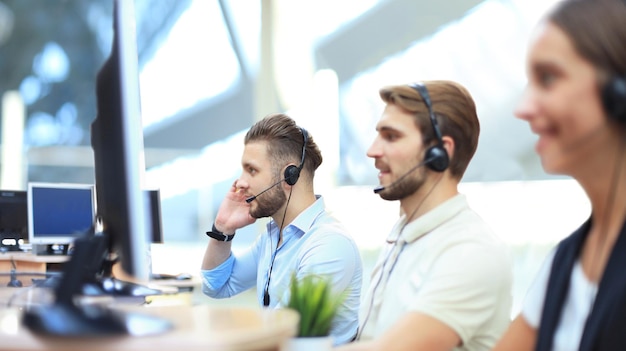 Porträt eines Call-Center-Mitarbeiters, begleitet von seinem Team. Lächelnder Kundendienstmitarbeiter bei der Arbeit.