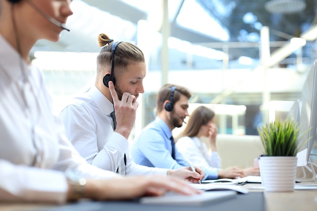 Porträt eines Call-Center-Mitarbeiters in Begleitung seines Teams. Lächelnder Kundendienstmitarbeiter bei der Arbeit.