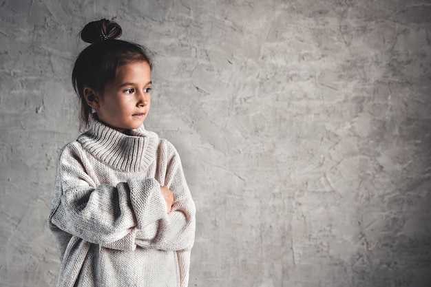 Porträt eines charmanten kleinen Mädchens im beigen Pullover auf grauem Hintergrund