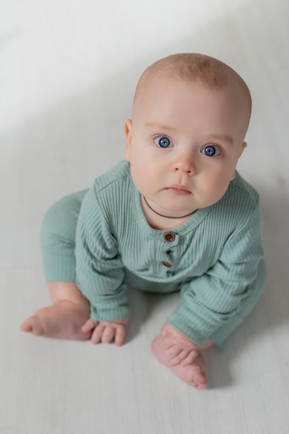 Porträt eines charmanten molligen Babys in einem grünen Overall, das auf der Draufsicht des Bodens sitzt