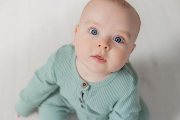 Porträt eines charmanten molligen Babys in einem grünen Overall, das auf der Draufsicht des Bodens sitzt