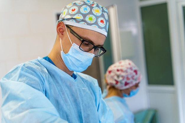 Porträt eines Chirurgen vor dem Operationssaal im Hintergrund. Männlicher Arzt trägt Maske. Junger Mediziner im Krankenhaus. Nahansicht.