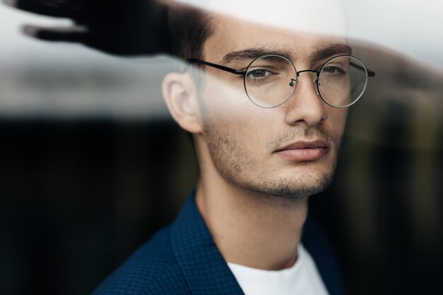 Foto porträt eines dunkelhaarigen jungen architekten mit brille in blau karierter jacke hinter dem glas.