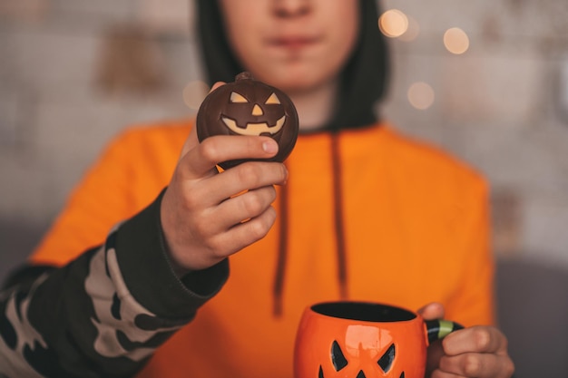 Porträt eines ehrlichen, authentischen Zoomer-Jungen, der mit einer Tasse Tee und Süßigkeiten zu Hause auf der Halloween-Party posiert