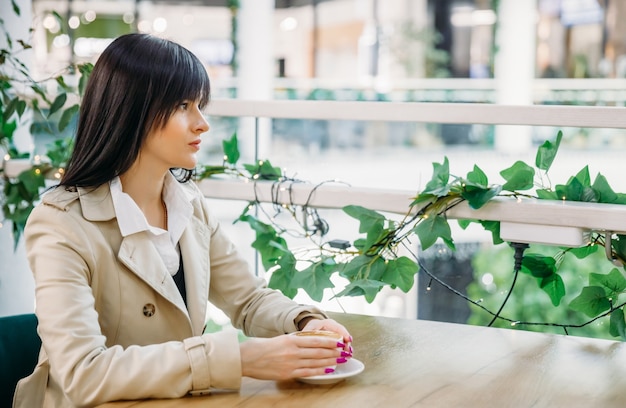 Porträt eines einsamen Mädchens in einem Café an einem Tisch mit einer Tasse Kaffee in den Händen