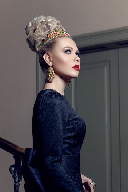 Porträt eines eleganten Modells im schwarzen Kleid mit abendlichem Make-up neben der Treppe