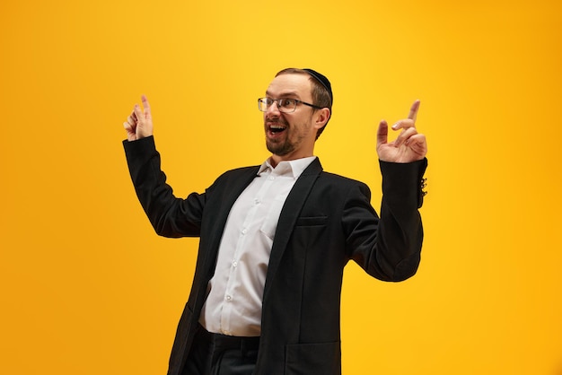 Porträt eines emotional aufgeregten jüdischen Mannes in schwarzem Anzug, der gegen ein gelbes Studio posiert
